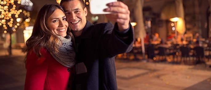 Couple takes a selfie in front of twinkle light lit courtyard